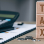 Blocks spell out tax on desk next to coins and a calculator