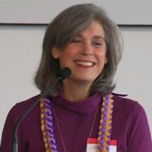 Sari Feinberg, White woman with shoulder length greying hair wearing a purple blouse