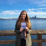 Allie Tripp holding her new book with the Seattle skyline in the background