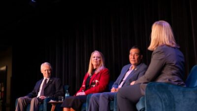 Panelists sit in chairs on stage