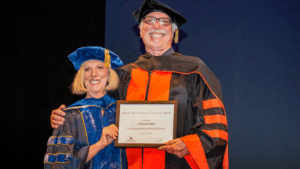 Pat smiling and holding award next to Dean Sandy Archibald