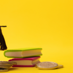 Graduation cap sits on stack of change next to globe and books