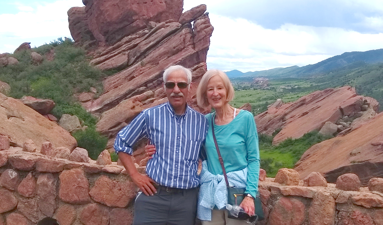 Bob and Melinda pose in front of a scenic view of red rocks and mountains in the distance