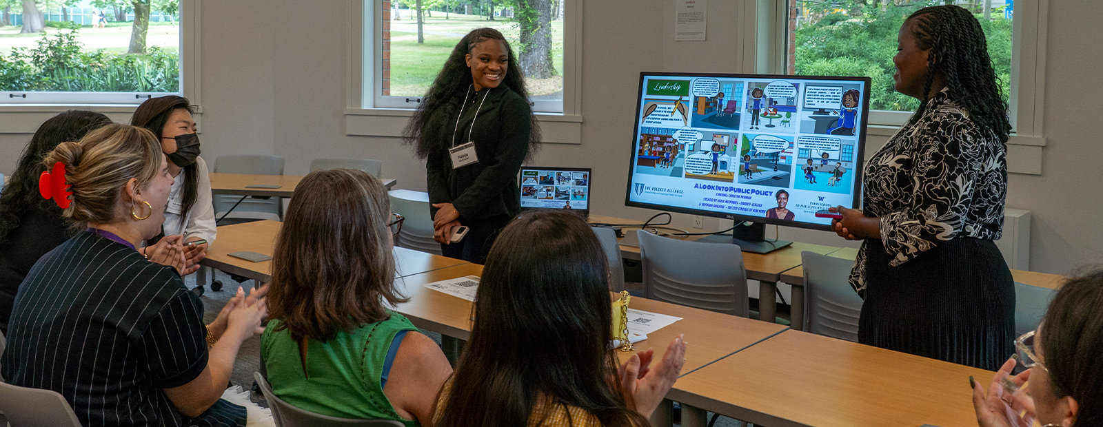 Two Evans Summer Policy Academy students are giving a presentation about public policy in the form of a comic to an audience of smiling people