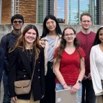 A group of students pose in front of a building with rainbow painted steps and the words "Kenmore City Hall" visible in the background