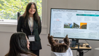 Two NextGen SPA students stand next to a screen with their presenation